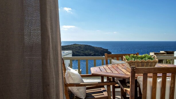 A wooden table and chairs on a balcony with a view of the sea and a distant island. - Ormos Seaside Villa G With Private Pool (Tinos)