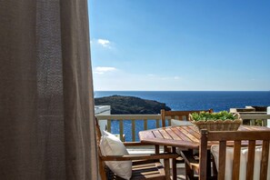 Ein Holztisch mit Stühlen auf einem Balkon mit Blick auf das Meer und eine entfernte Insel.
