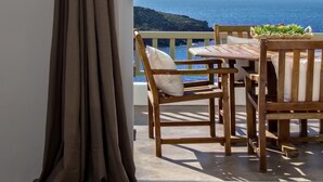 A balcony with a wooden table and chairs, a view of the sea, and a large bed. - Ormos Seaside Villa G With Private Pool (Tinos)