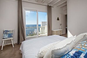 A bedroom with a large bed, a chair, a nightstand, and a view of the sea. - Ormos Seaside Villa G With Private Pool (Tinos)