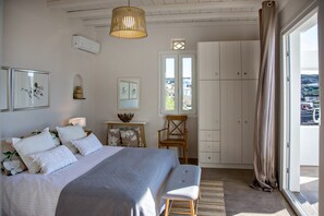 A bedroom with a bed, a window with a view, a wardrobe, and a desk with a lamp. - Ormos Seaside Villa G With Private Pool (Tinos)