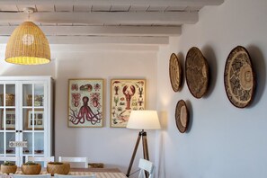 A dining area with a white table, wicker baskets, and a hanging pendant light. - Ormos Seaside Villa G With Private Pool (Tinos)