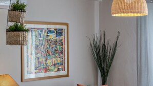 A modern living room with a grey sofa, a hanging woven lamp, a framed abstract painting, and a tall plant. - Ormos Seaside Villa G With Private Pool (Tinos)