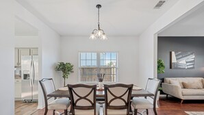 Un comedor con una mesa y sillas de madera, una lámpara colgante y un ventanal con persianas.
