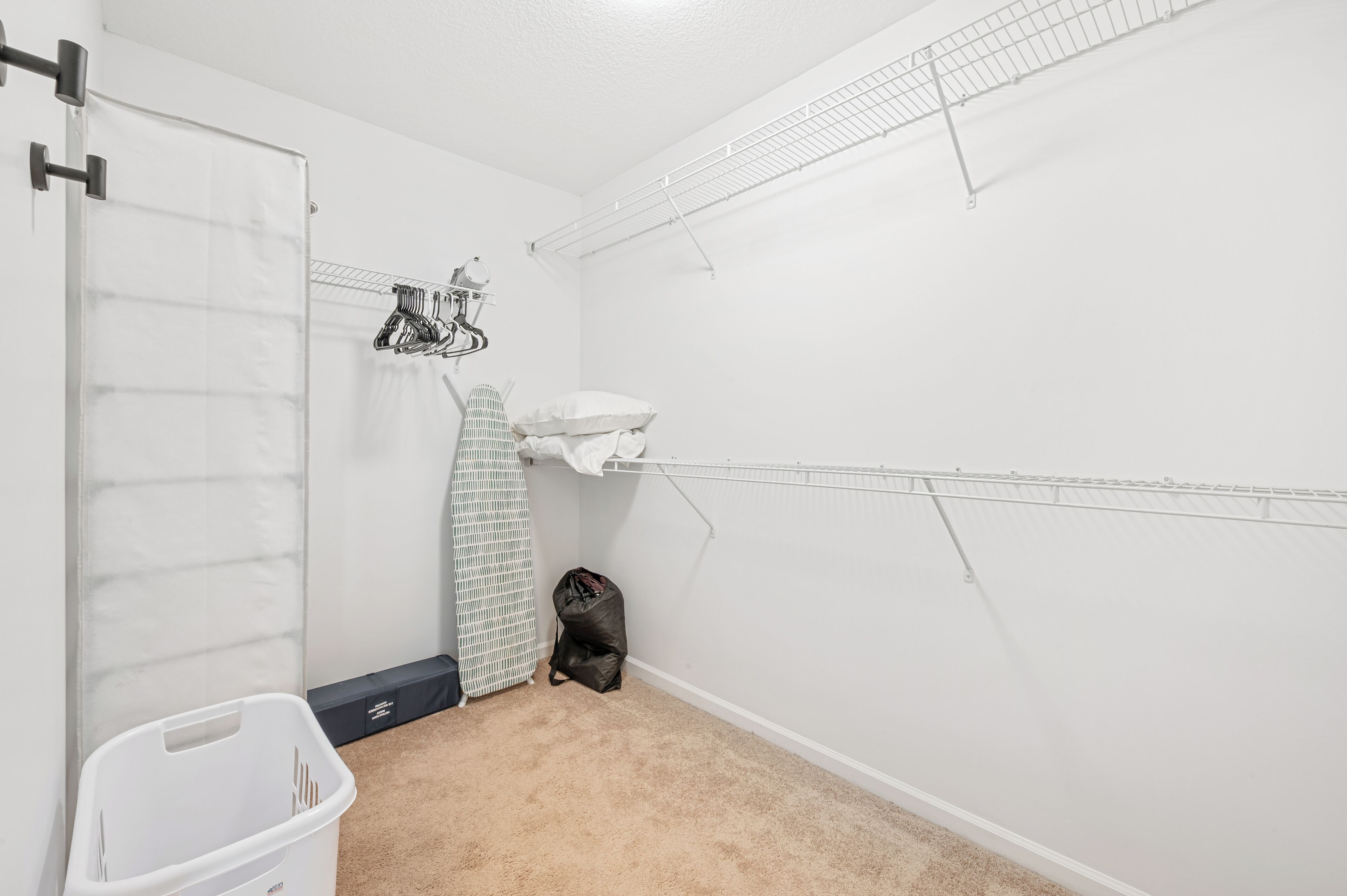 A laundry room with a white door, a drying rack, a basket, and a trash bin.