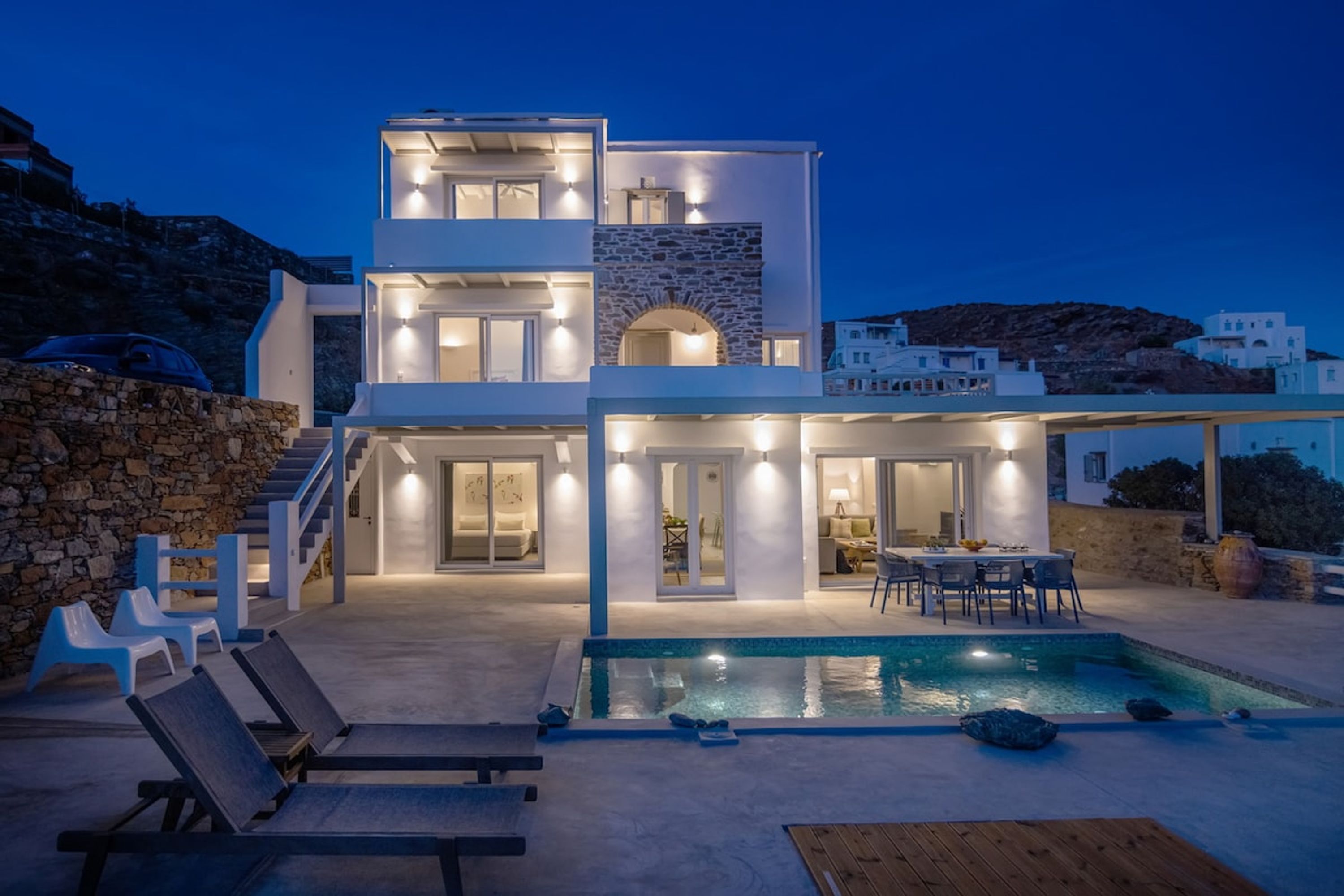 Une maison moderne à deux étages, dotée d’une piscine, d’un espace salon extérieur et d’un mur en pierre.