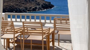 Eine Terrasse mit Holzbänken und einem Tisch, mit Blick auf eine felsige Küstenlinie und das Meer.