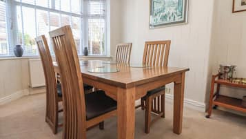 A dining area with a wooden table and chairs, large windows with blinds, and a framed picture on the wall.