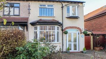 A two-story house with a bay window, a front door, and a small garden area with potted plants.