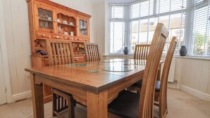 Comedor con mesa y sillas de madera, un mueble de madera con puertas de cristal y vistas amplias por ventanas grandes.