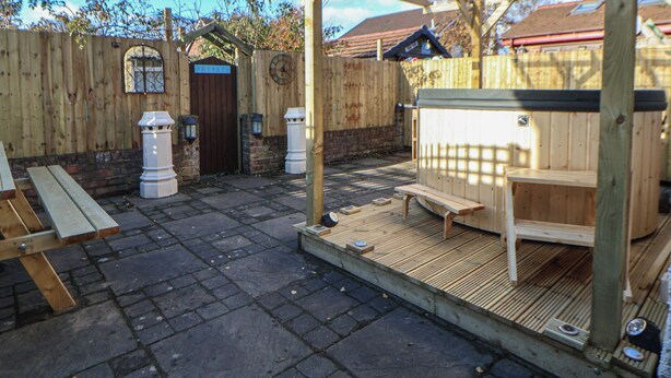 Una terraza de madera con un jacuzzi, bancos de madera y una estructura de pérgola.