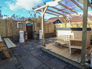 Eine Holzterrasse mit Whirlpool, Holzbanken und einer Pergola.
