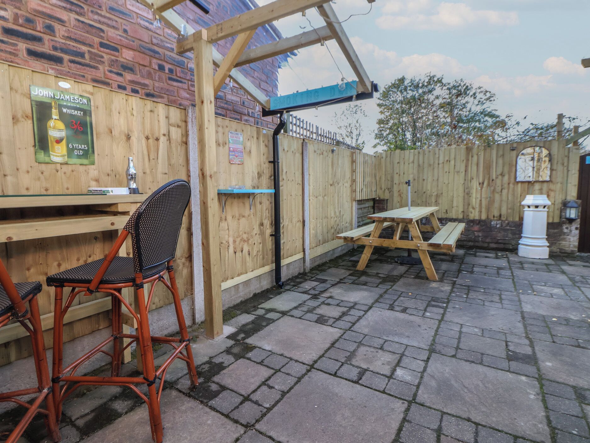 A wooden outdoor seating area with a table and chairs, a wooden fence, and a brick wall.