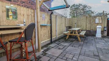 A wooden outdoor seating area with a table and chairs, a wooden fence, and a brick wall.
