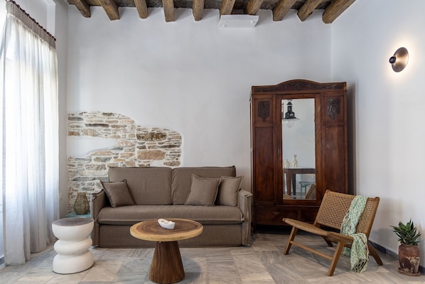 A cozy living room with a stone wall, a wooden cabinet, a sofa, a round table, and a rattan chair.