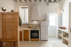 A compact kitchen with a built-in oven, a refrigerator, and a window with curtains.