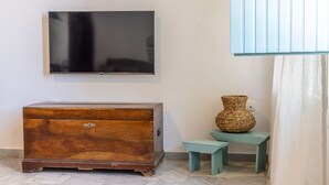 Ein Zimmer mit einer Holzkistenkommode, einem wandmontierten Flachbildfernseher, einem Korbwannenkorb auf einem kleinen Hocker und einem blauen Schrank.