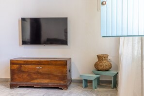 A room with a wooden chest of drawers, a television mounted on the wall, a small table with a woven basket, and a blue cabinet.