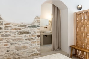 A stone wall, a white sink, a mirror, and a wooden bench in a bathroom.
