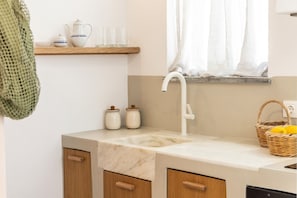 Una cocina con encimera de mármol, armarios de madera, un lavamanos blanco y una ventana con cortinas ligeras.