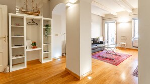 Una sala de estar moderna con piso de madera, una mesa de centro de vidrio, un tapete rojo y una estantería con una maqueta de barco.
