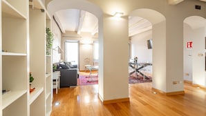 Amplia sala de estar con piso de madera, paredes blancas y un área central con sofá y mesa de centro.