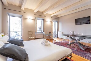 Moderni hotellihuone, jossa on suuri sänky, ruokapöytä ja seinälle asennettu televisio.