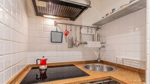 Une cuisine avec des murs recouverts de carreaux blancs, une plaque de cuisson à induction noire, un évier en acier inoxydable et divers ustensiles de cuisine suspendus à un porte-ustensiles.