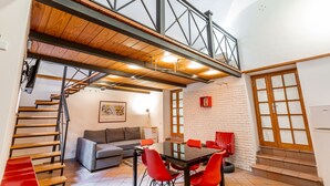 Un intérieur moderne avec un escalier menant à une mezzanine, un coin repas avec des chaises rouges et un canapé gris.