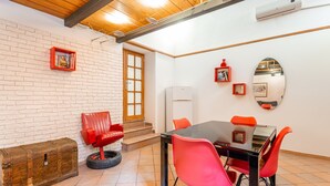 Une pièce avec un mur en briques blanches, un plafond en bois, une table en verre avec des chaises rouges, un fauteuil en cuir rouge, une commode en bois et un climatiseur blanc.