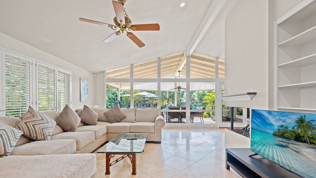 A spacious living room with a large TV, a ceiling fan, and a view of the outdoors through large windows. - Bright Family Getaway Large Backyard Oasis Patio (Santa Ana)