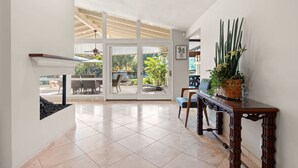 A spacious hallway with a view to an outdoor patio area, a wooden console table with potted plants, and a ceiling with exposed beams. - Bright Family Getaway Large Backyard Oasis Patio (Santa Ana)