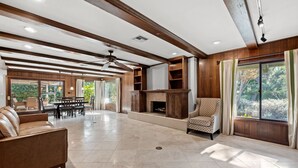 A spacious living room with a fireplace, wooden beams, and a large window with curtains. - Bright Family Getaway Large Backyard Oasis Patio (Santa Ana)