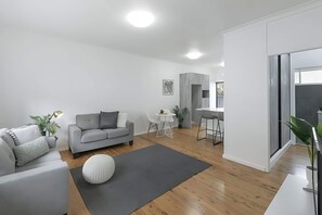 A modern living room with a grey sofa, a round white ottoman, and a small round table with a plant. - Prickly Pear Stays in Adamstown, 1-br (Newcastle)