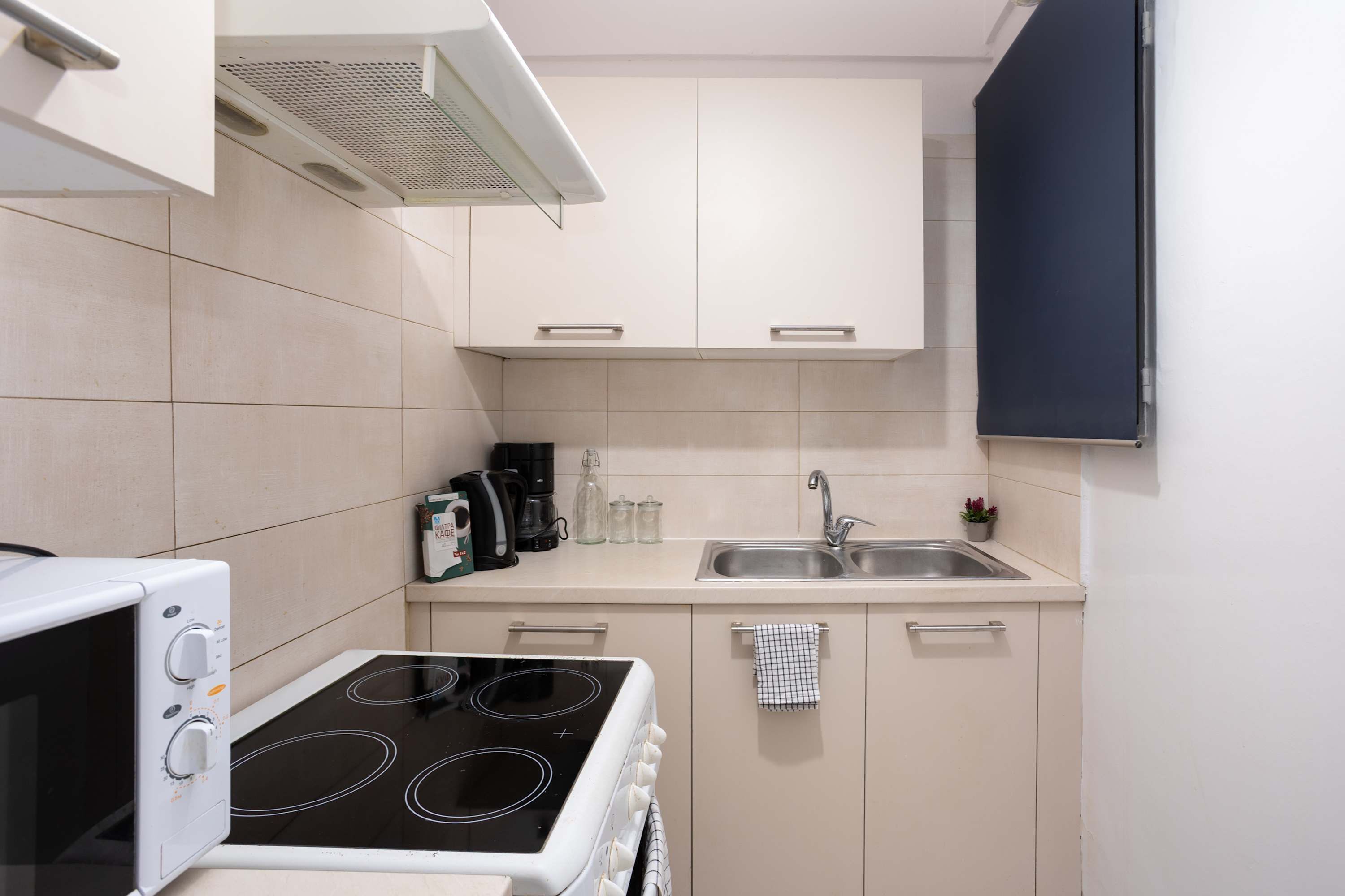 Een kleine keuken met een kookplaat, magnetron, spoelbak en kastjes.