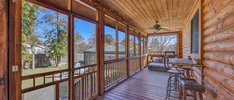A wooden deck with a covered area, large windows, and outdoor seating.
