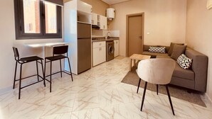 Um espaço compacto com cozinha compacta, área de refeições para dois, sofá com almofadas e janela com persianas.