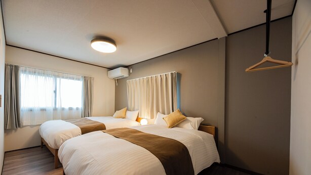 A hotel room with two beds, a ceiling light, a window with curtains, and a hanging coat rack.