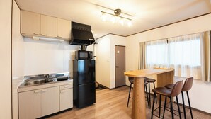 A compact kitchen with a refrigerator, microwave, and a wooden dining table with chairs.