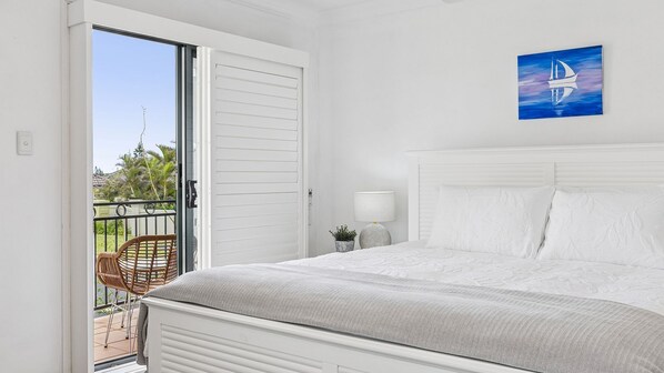 A bedroom with a bed, a nightstand, a lamp, and a painting of a sailboat.