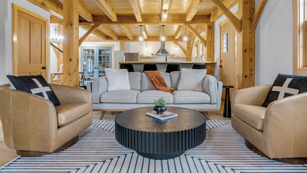 A cozy living room with a wooden ceiling, a round coffee table, and two leather sofas with cushions. - Timberframe Cabin with Hot Tub Close to Sunday River! (Bethel)