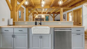 A kitchen with wooden beams, a central island with a sink, and a Bosch dishwasher. - Timberframe Cabin with Hot Tub Close to Sunday River! (Bethel)