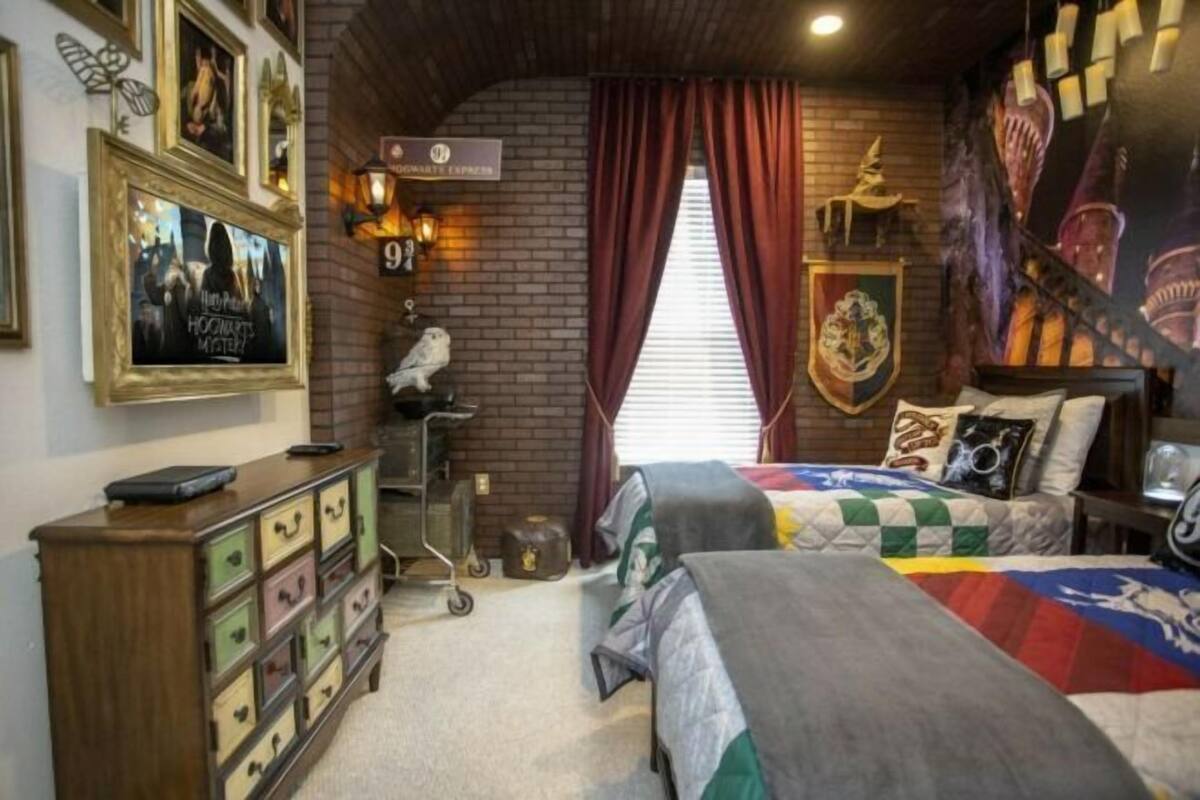 A themed room with a brick wall, a sign reading "9th Hogwarts Express," a bed with a colorful quilt, a wooden dresser with multiple drawers, and a wall adorned with framed pictures and a shield emblem.
