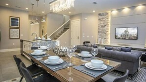 A modern dining area with a wooden table set for four, a grey sofa, and a staircase leading to an upper level. - Summerville Resort 5 Bedroom Vacation Home 2620 (Kissimmee)
