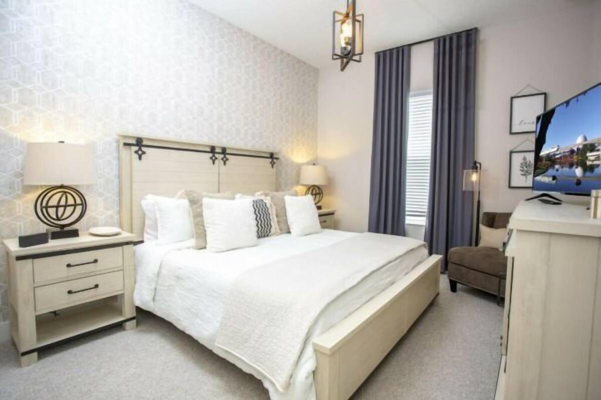 A hotel room with a large bed, bedside tables, a TV, and a wardrobe.