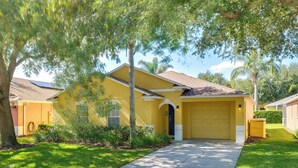 A yellow house with a garage, surrounded by greenery and a clear sky. - Peaceful Clermont Gem w/ Pool, 9 Mi to Disney! (Clermont)