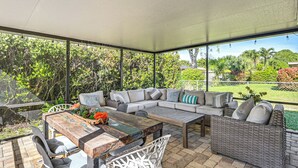 Eine Terrasse im Freien mit einem Holztisch, weißen Stühlen, einer Couch und einem Korbsessel.