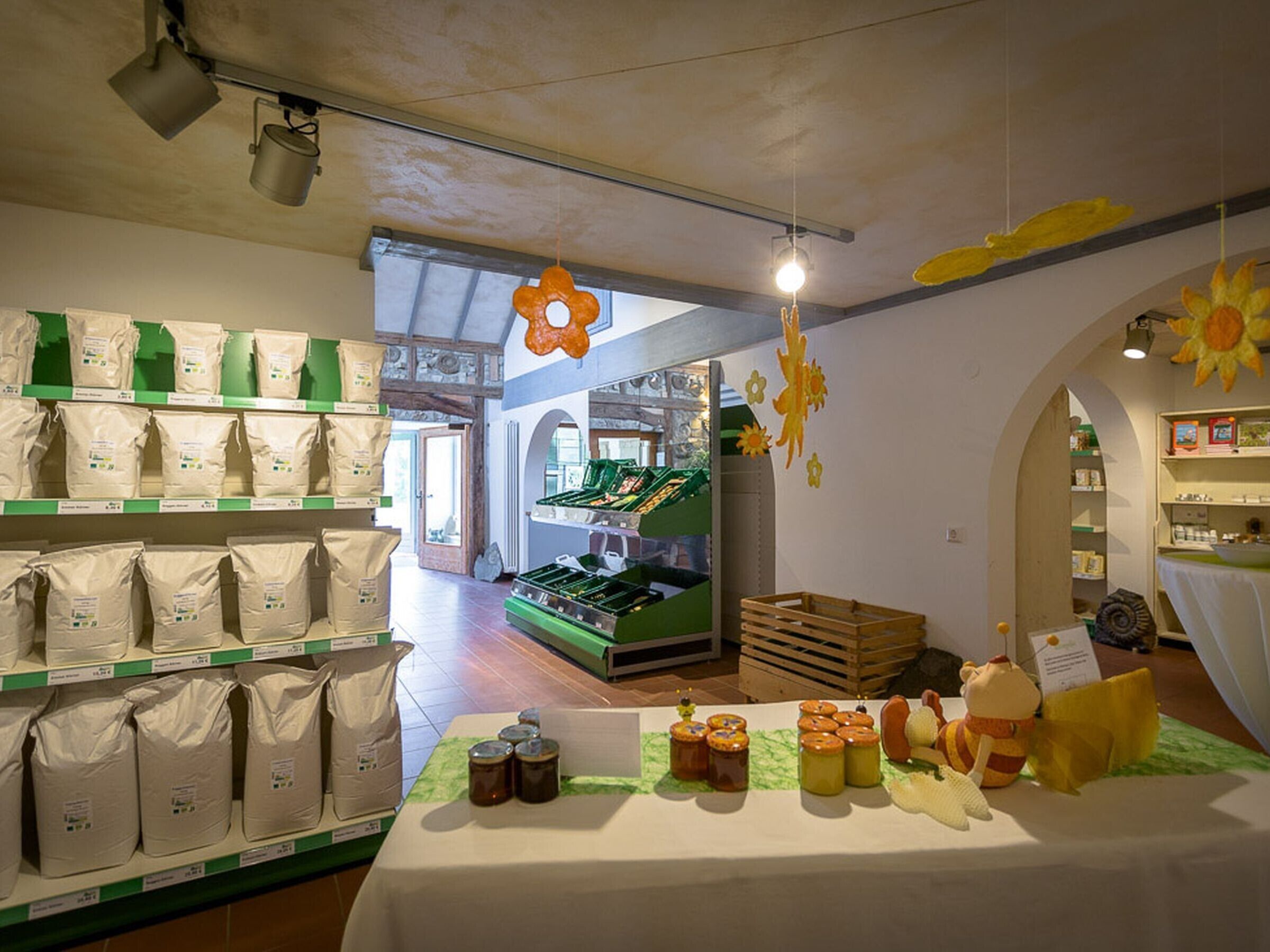 A store with shelves of bags and jars, a display table with jars and a stuffed toy, and a green crate in the background.