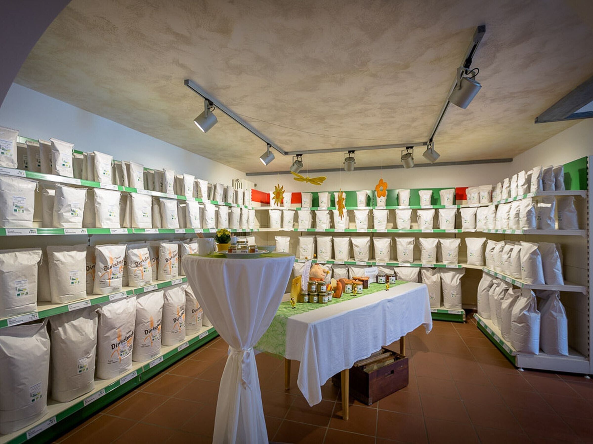 Une pièce de rangement avec des étagères remplies de sacs, une table avec des bocaux et un ventilateur au plafond.