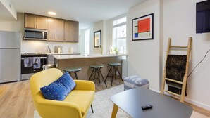 A modern kitchen with wooden cabinets, a microwave, and a stove. There is a yellow armchair with a blue pillow, a small table with a remote control, and a ladder against the wall. - 1 Mi to University of Cincinnati: 3rd-floor Condo! (Cincinnati)